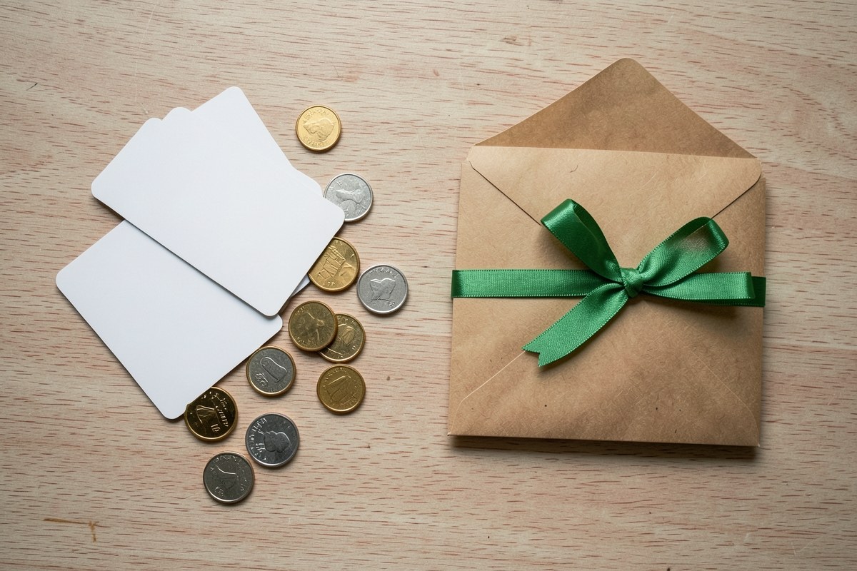 Several scattered credit cards and coins being swept into a single open envelope on a table.